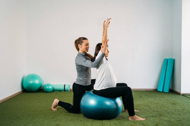 Pregnant woman doing fitness ball and pilates exercise with coac - Foto, imagen