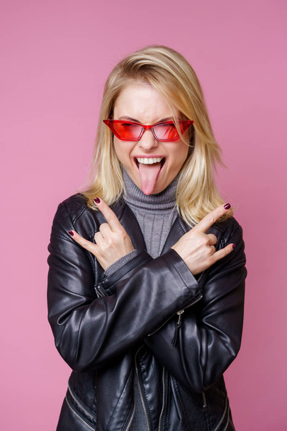 Image of blonde in pink glasses and leather jacket showing tongue - Zdjęcie, obraz