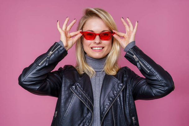 Photo of blonde in pink glasses and leather jacket with hands near face - 写真・画像