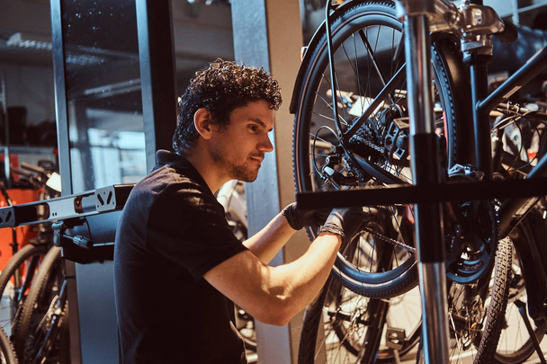 Attractive mechanic is fixing customers bicycle at his own workshop. - Фото, зображення