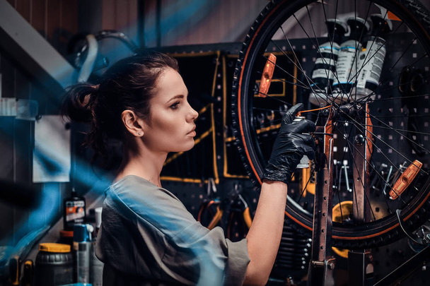 Diligent beautiful girl is repairing bicycle at busy workshop between pneumatic wires - Photo, Image