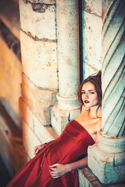 Bridesmaid girl at wedding ceremony in castle. Woman at stone ancient column in summer. Wedding fashion and beauty. Fashion model or princess in dress. Sexy girl in red dress with stylish hair. - Foto, Imagen