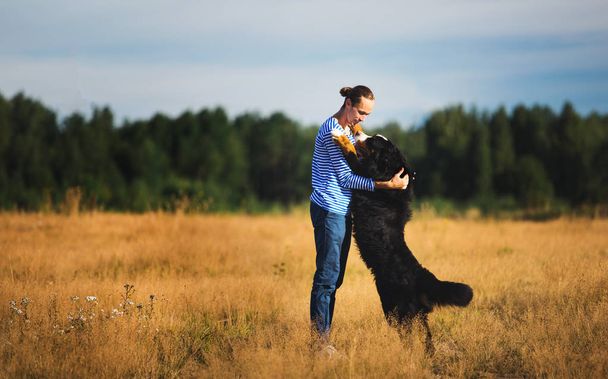 young man walking with Bernese Mountain Dog on the summer field - Фото, изображение