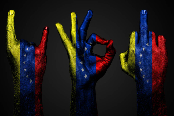 un conjunto de tres manos con una bandera pintada Venezuela mostrar el dedo medio, cabra y bien, un signo de agresión, protesta y aprobación sobre un fondo oscuro
. - Foto, imagen