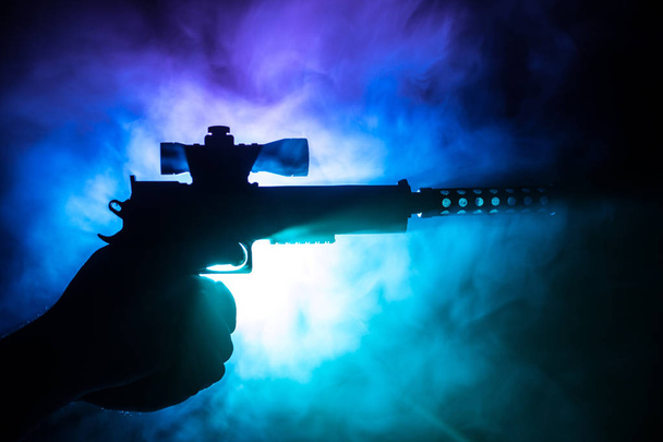Pistola a mano maschile su sfondo nero con luci posteriori color fumo. La sagoma di una pistola in mano. Concetto di crimine. Focus selettivo
 - Foto, immagini