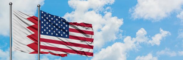 一緒に白い曇り青い空に対して風に手を振るバーレーンと米国の旗。外交概念、国際関係. - 写真・画像