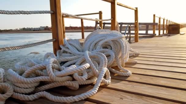 4k felvételt a hosszú, fából készült mólón naplementekor sugarak. A fa fedélzetén fekvő fehér kötelek és kábelek - Felvétel, videó
