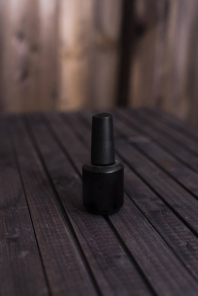 musta pullo geeliä kynsilakka puupohjalla. Musta lakka kauniilla taustalla
 - Valokuva, kuva