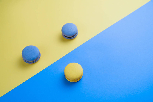 Sweet tasty blue and yellow french macaron cakes on yellow and blue background. - Fotografie, Obrázek