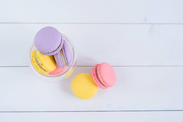 Delicious colorful macarons in a transparent glass cup on white wooden background. - Foto, imagen