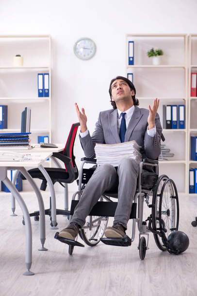 Giovane bel dipendente in sedia a rotelle che lavora in ufficio   - Foto, immagini