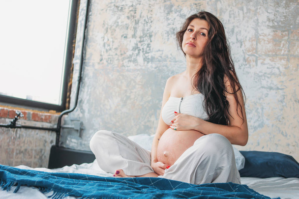 Bella ragazza incinta giovane donna con lunghi capelli ricci seduta in posa loto sul letto. Gravidanza yoga e natura concetto di bellezza etnica
 - Foto, immagini
