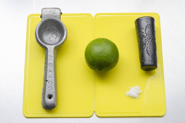 Squeezer, lemon, salt and tequila shot glass on a yellow cooking table - Photo, Image