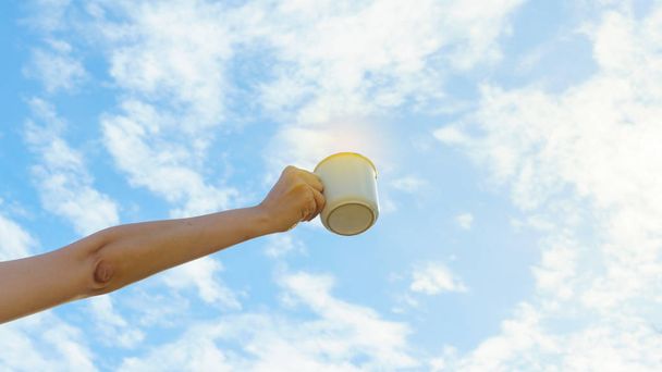 asiatische Frauenhände halten heißen Kaffeebecher im Freien auf klarem Himmelshintergrund mit Kopierraum. Kaffee am Morgen genießen. - Foto, Bild