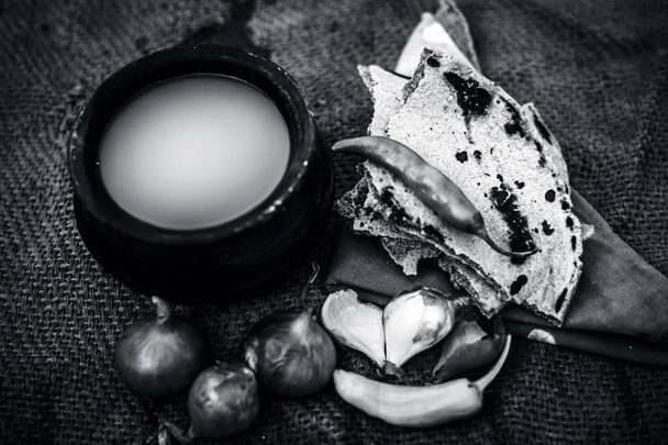 Close up of meal or lunch of villager or a typical farmer on gunny bag's background consisting of pearl millet's roti or chapati or bajra or bajri ki roti with some onions and chilies, buttermilk . black and white - Foto, Imagen