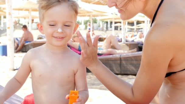 wideo 4K szczęśliwej rodziny stosując balsam UV ochrony przed słońcem na plaży morskiej w gorący słoneczny dzień - Materiał filmowy, wideo