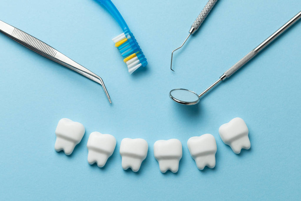 Zdravé bílé zuby na modrém pozadí a nástroje zubaře, hák. - Fotografie, Obrázek