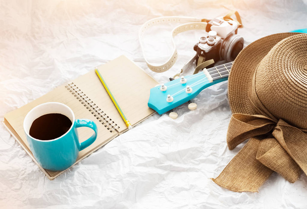 La taza de café de cerámica se puso en la cámara book.beside marrón, ukelele y hat.accessories tejido para relajarse viaje, luz borrosa alrededor
 - Foto, Imagen