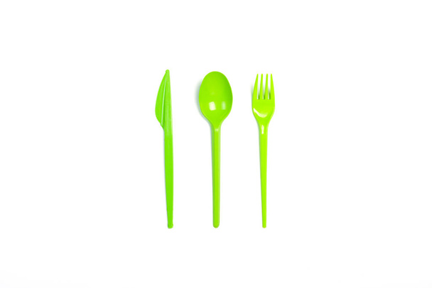Zelené plastové nádobí a přístroje na jedno použití pro potraviny na bílém podkladu. Vidlička, lžíce a nůž. Koncepce plastická, škodlivá, znečištění životního prostředí, stop plastická. Plochý, pohled shora. - Fotografie, Obrázek