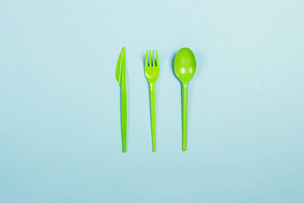 Groene wegwerp plastic servies en apparaten voor voedsel op een blauwe achtergrond. Vork, lepel en mes. Concept plastic, schadelijk, milieuvervuiling, stop plastic. Platte lay, bovenaanzicht. - Foto, afbeelding