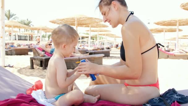 4k slow motion vídeo of young caring mother applying sunscreen lotion on her toddler son at sea beach
 - Filmagem, Vídeo