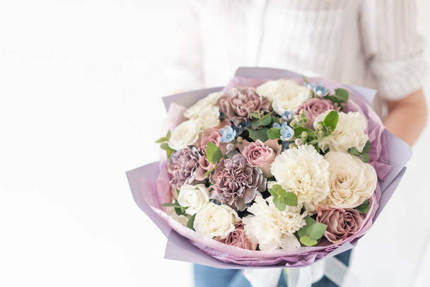 Όμορφη ανθοδέσμη από ανάμεικτα λουλούδια στο χέρι της γυναίκας. το έργο του ανθοπώλη σε ένα ανθοπωλείο. Λεπτό παστέλ χρώμα. Φρεσκοκομμένο λουλούδι. Λευκό και λιλά χρώμα - Φωτογραφία, εικόνα