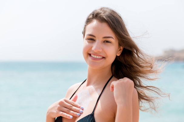Krásná žena na prsou používá krém s prsty na pozadí moře - Fotografie, Obrázek