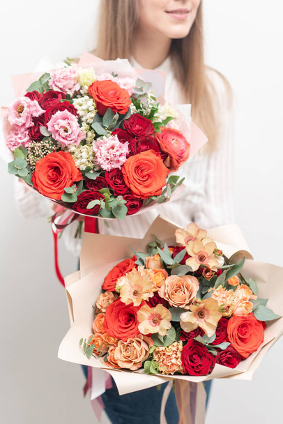 δύο όμορφα Μπουκέτα από ανάμεικτα λουλούδια σε γυναίκες χέρια. το έργο του ανθοπώλη σε ένα ανθοπωλείο. Λεπτό παστέλ χρώμα. Φρεσκοκομμένο λουλούδι. Κόκκινο και ροδάκινο χρώμα - Φωτογραφία, εικόνα