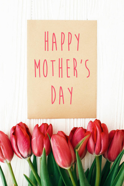 fröhlicher Muttertagstext und schöne rote Tulpen auf weißem Holz - Foto, Bild