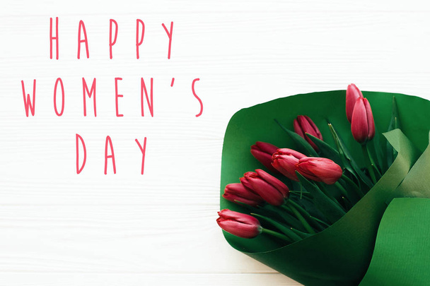 fröhlicher Frauentagstext und schöne rote Tulpen auf weißem Holz  - Foto, Bild