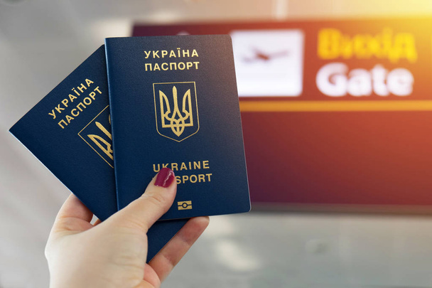 Kaksi ukrainalaista biometristä passia kädessä. Lentoaseman opasteet taustalla
. - Valokuva, kuva