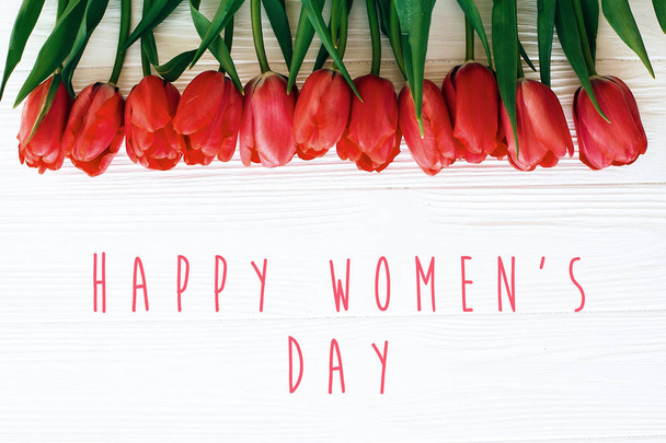 Ευτυχισμένο το κείμενο της ημέρας της γυναίκας και όμορφες κόκκινες τουλίπες σε λευκό ξύλινο  - Φωτογραφία, εικόνα