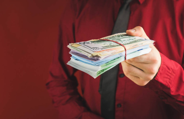 maços de dinheiro nas mãos de um homem de terno vermelho em um fundo vermelho
 - Foto, Imagem