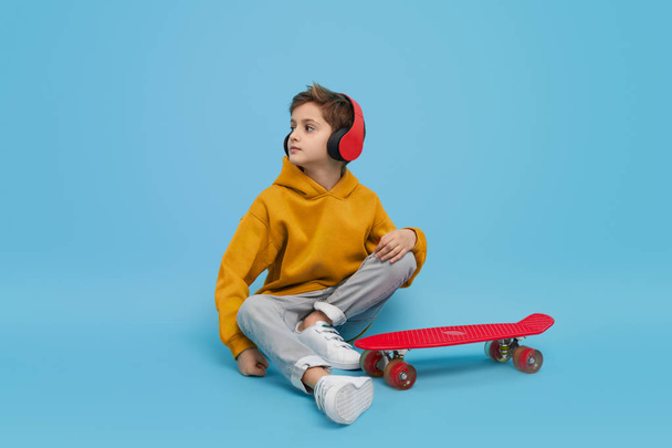 Stylish youngster listening to music near longboard - 写真・画像
