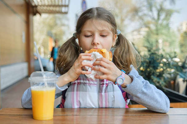 Portrait of girl student with backpack, eating burger with orange juice, background of outdoor fast food cafe - Valokuva, kuva