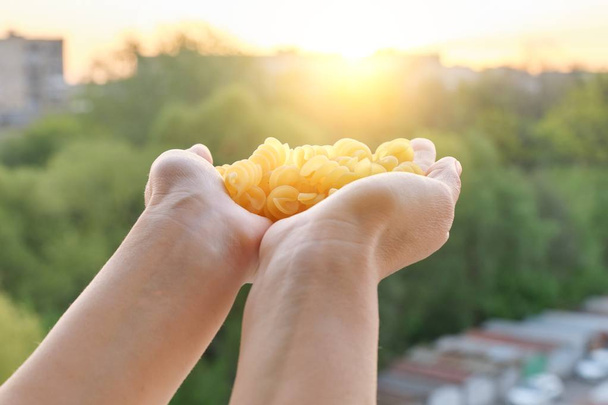 Spiral pasta, close-up of hands holding pasta, background sunset sky golden hour - Photo, image
