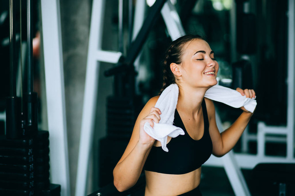 Young attractive woman caucasian sitting and using towel to wipe the sweat. Relaxation after hard workout in gym. Fitness concept, Healthy, Sport, Lifestyle - Foto, Imagem