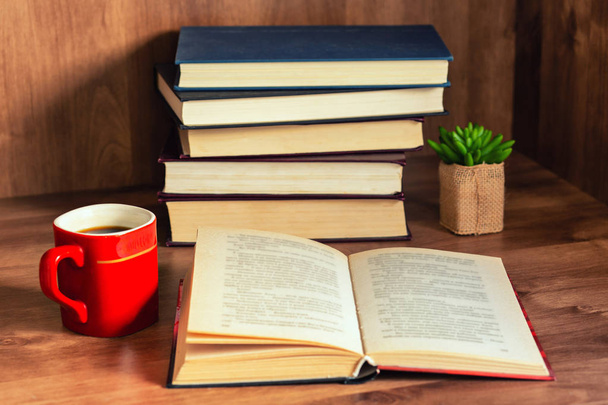 Pilha de livros fechados e livro aberto com xícara de café em fundo de madeira
. - Foto, Imagem