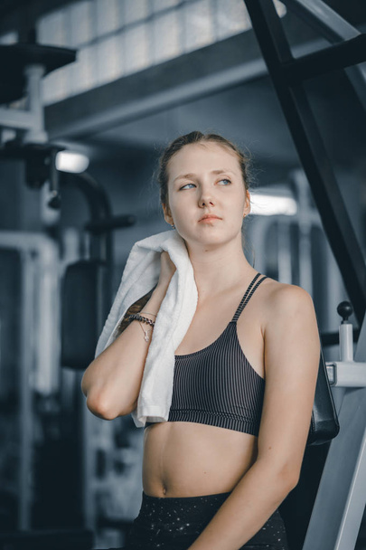 Young attractive woman caucasian sitting and using towel to wipe the sweat. Relaxation after hard workout in gym. Fitness concept, Healthy, Sport, Lifestyle - Fotografie, Obrázek