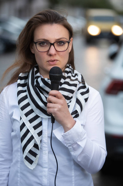 young woman standing on street with microphone and talking - 写真・画像