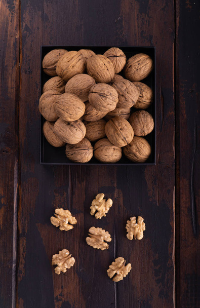 Whole and cracked walnuts on a square plate on wooden table, top view. Healthy nuts and seeds composition. - Фото, зображення