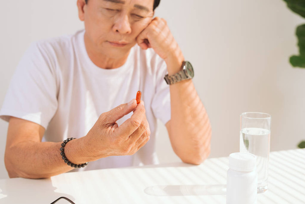 Sad unhappy senior man taking pills while sitting at home. - Фото, зображення