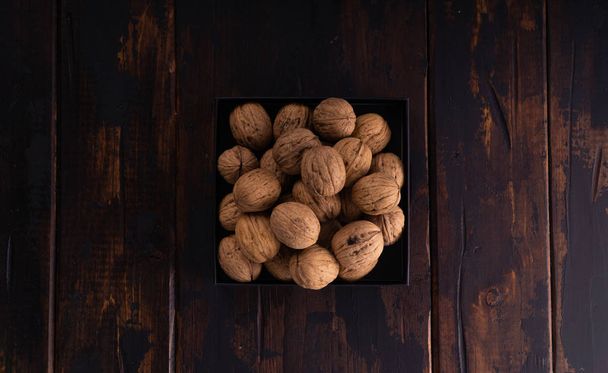 Whole walnuts on a square plate on wooden table, top view. Healthy nuts and seeds composition. - Fotó, kép