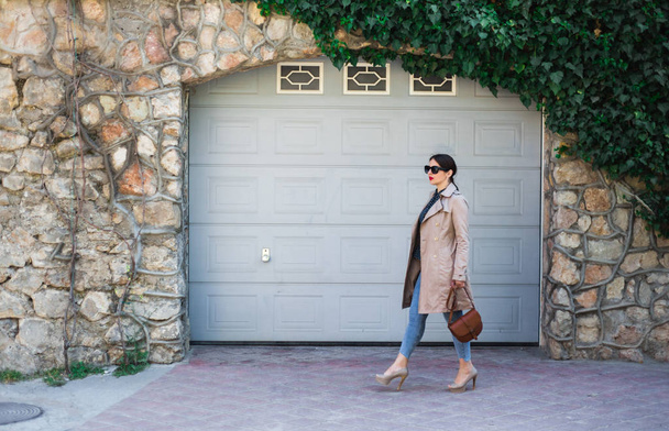 Mulher bonita vestindo jeans e trincheira, de pé contra a parede na rua da cidade. Moda casual, elegante look diário
. - Foto, Imagem