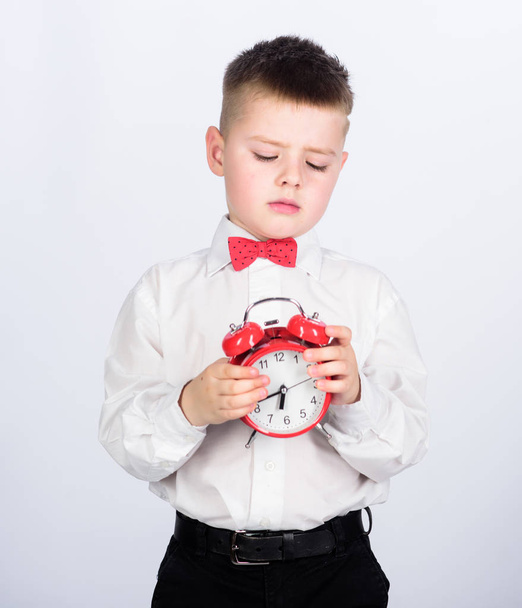 Develop self discipline. Set up alarm clock. Child little boy hold red clock. It is time. Schedule and timing. Morning routine. Schoolboy with alarm clock. Kid adorable boy white shirt red bow tie - Photo, Image
