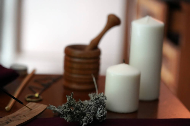 A sprig of wormwood for magic on the background of white extinguished candles, a wooden mortar and an amulet on the table. Occult, esoteric, divination and Wicca concept. - Photo, Image