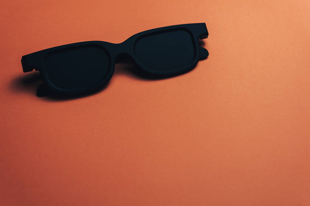 Μαύρο κλασικό γυαλιά σε ένα πανέμορφο κοραλλιογενές πορτοκαλί φόντο. - Φωτογραφία, εικόνα