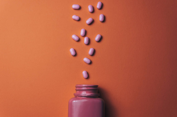 Красива рожева пляшка і рожеві таблетки на красивому кораловому помаранчевому фоні
.  - Фото, зображення