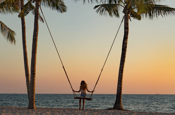 Концепция отпуска. Молодая женщина качается на пляжных качелях. Счастливые путешественницы на пляже Фу Куок
 - Фото, изображение