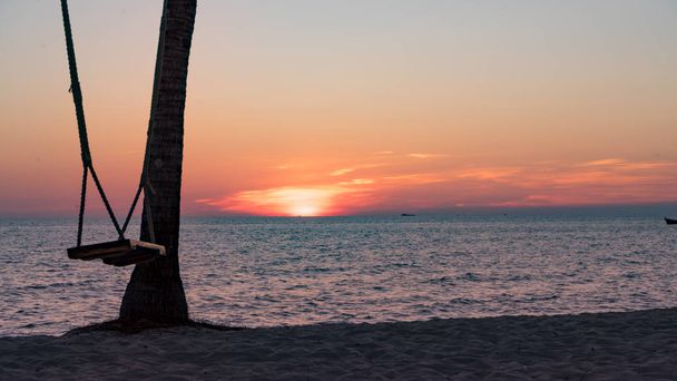 Swing en la hermosa playa con hermosa puesta de sol naranja con arena blanca y fondo de agua cristalina azul para el concepto de turismo
 - Foto, imagen